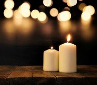 Two lit candles on wooden surface, blurred lights background.