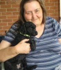 Person smiling, holding small black dog.