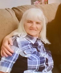 Woman smiling, sitting on couch with plaid shirt.