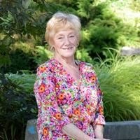 Smiling person in floral blouse outdoors with greenery