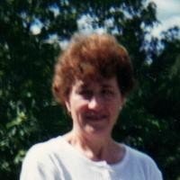 Woman smiling outdoors with trees in background.