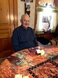 Smiling man sitting by birthday cake on table.