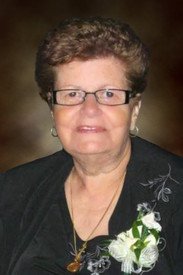 Elderly woman with glasses and floral attire.