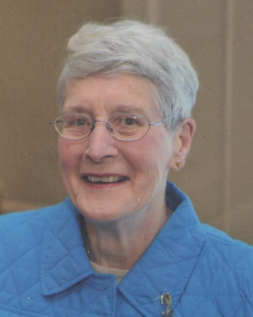 Smiling woman in blue jacket with glasses.