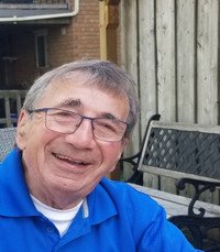 Smiling man in blue shirt sitting outside.
