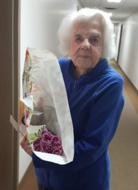 Elderly person holding flower bouquet in hallway.