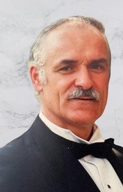 Man in tuxedo with a mustache and gray hair.
