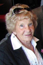 Elderly woman smiling indoors, wearing sunglasses on head.