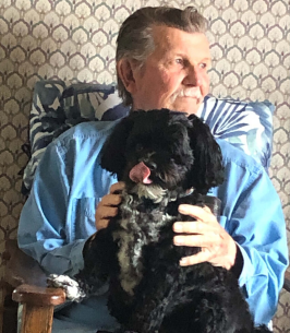 Man with black dog on lap, sitting indoors.