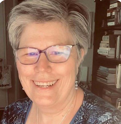 Smiling person wearing glasses near bookshelves.