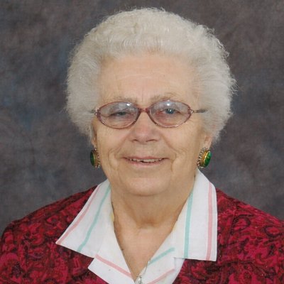 Elderly person smiling with glasses and red jacket.
