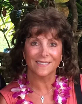 Smiling woman wearing floral lei outdoors.