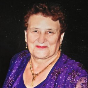Elderly woman smiling in purple attire.