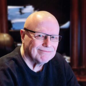 Smiling person with glasses and black shirt indoors.