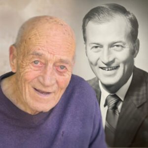 Elderly man with younger portrait in background.