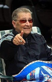 Smiling person pointing, wearing sunglasses and jacket.