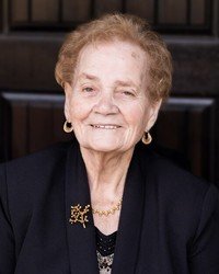 Elderly woman smiling in formal attire.