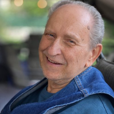 Smiling elderly man, blue jacket outdoors.