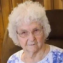 Elderly woman with white hair and glasses.