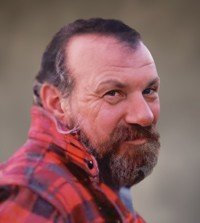 Man in plaid shirt with beard, smiling.