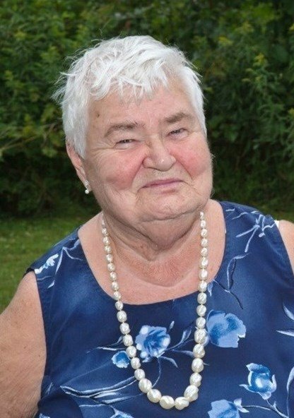 Smiling elderly woman in blue floral dress outside.