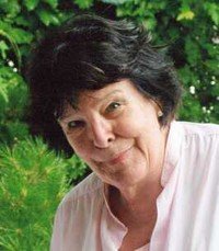 Smiling woman with dark hair, greenery background.