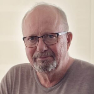 Elderly man with glasses and beard smiling indoors.
