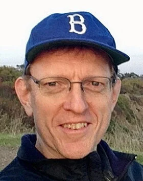 Man wearing glasses and blue cap outdoors.