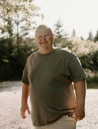 Smiling person stands outdoors in sunlight.