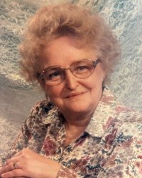 Smiling elderly woman wearing floral blouse and glasses.