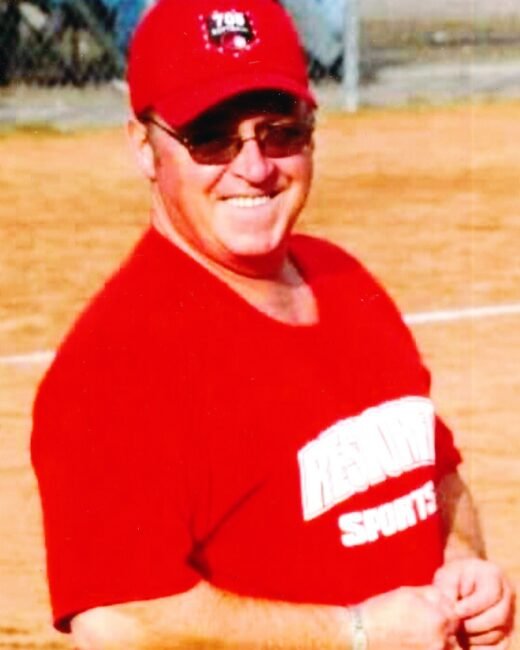 Smiling man in red sports cap on field.