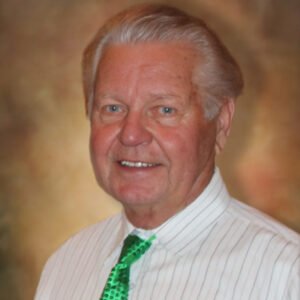 Man in white shirt with green tie, smiling.
