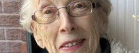 Elderly woman smiling with glasses and short hair.