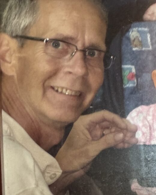 Smiling person with glasses and short gray hair.
