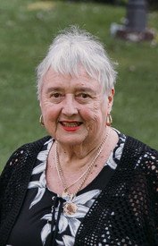 Elderly woman smiling outdoors with short white hair.