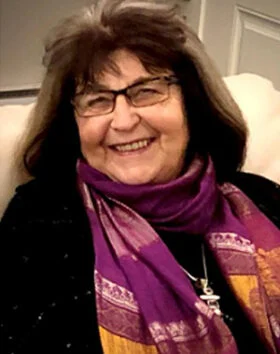 Smiling woman with glasses and scarf seated indoors.