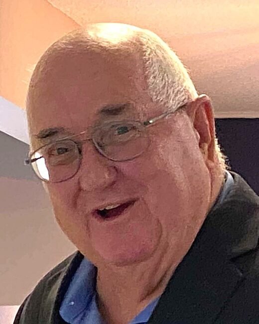 Man smiling indoors with glasses and suit jacket.