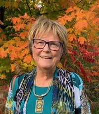 Person smiling in front of autumn leaves.