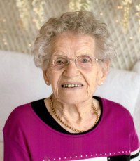 Elderly woman with glasses, smiling indoors.