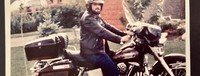 Man on motorcycle in leather gear outside home.