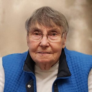Elderly person wearing blue vest and glasses.