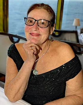 Smiling woman in glasses, black dress, dining setting.