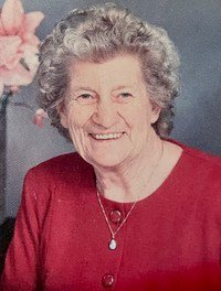 Smiling elderly woman in red with gray hair.
