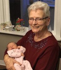 Elderly woman holding sleeping newborn baby indoors.