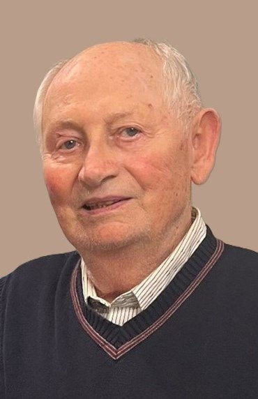 Elderly man smiling in a sweater and shirt.