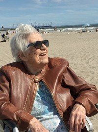 Elderly woman smiling on a sunny beach day.