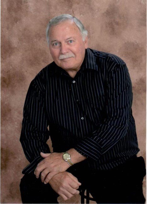 Older man in black shirt sitting, brown background.