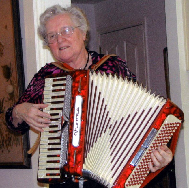 HENTSCHEL, Ilse Charlotte Elisabeth Hentschel Elderly woman playing a red accordion indoors.