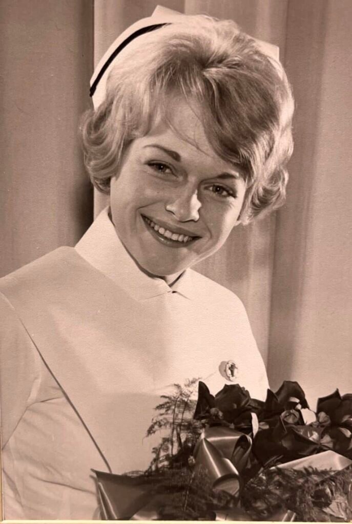 Smiling nurse in vintage uniform holding flowers.