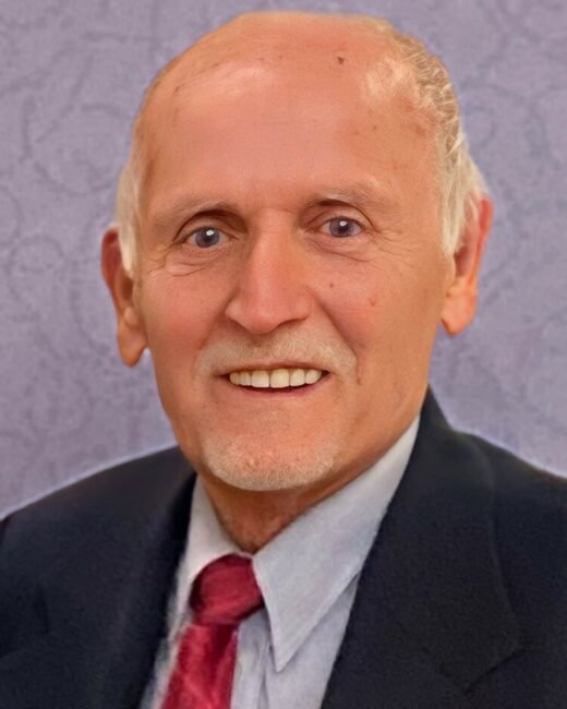 Elderly man smiling in suit and tie.